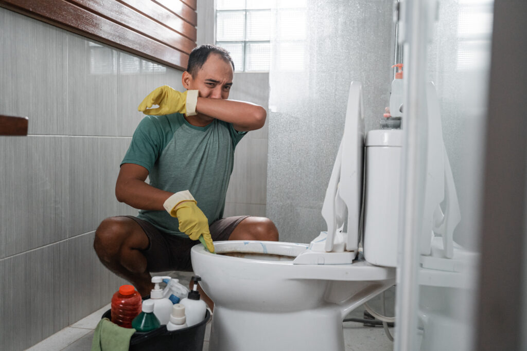 Homeowner covering nose as he cleans toilet that smells like sewer gasses.