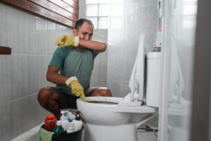 Homeowner covering nose as he cleans toilet that smells like sewer gasses.
